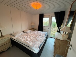 Une chambre à coucher avec un lit, des tables de chevet, une lampe, une commode et une fenêtre avec des rideaux.