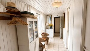 A corridor with a wooden cabinet, wicker chairs, and a hanging hat rack. - Panoramic ocean view, direct access to a private sandy beach in Skagen South—family-friendly (Ålbæk)