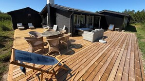 A wooden deck with outdoor furniture, including chairs and a table, and a covered seating area with a sofa and chairs. - Panoramic ocean view, direct access to a private sandy beach in Skagen South—family-friendly (Ålbæk)
