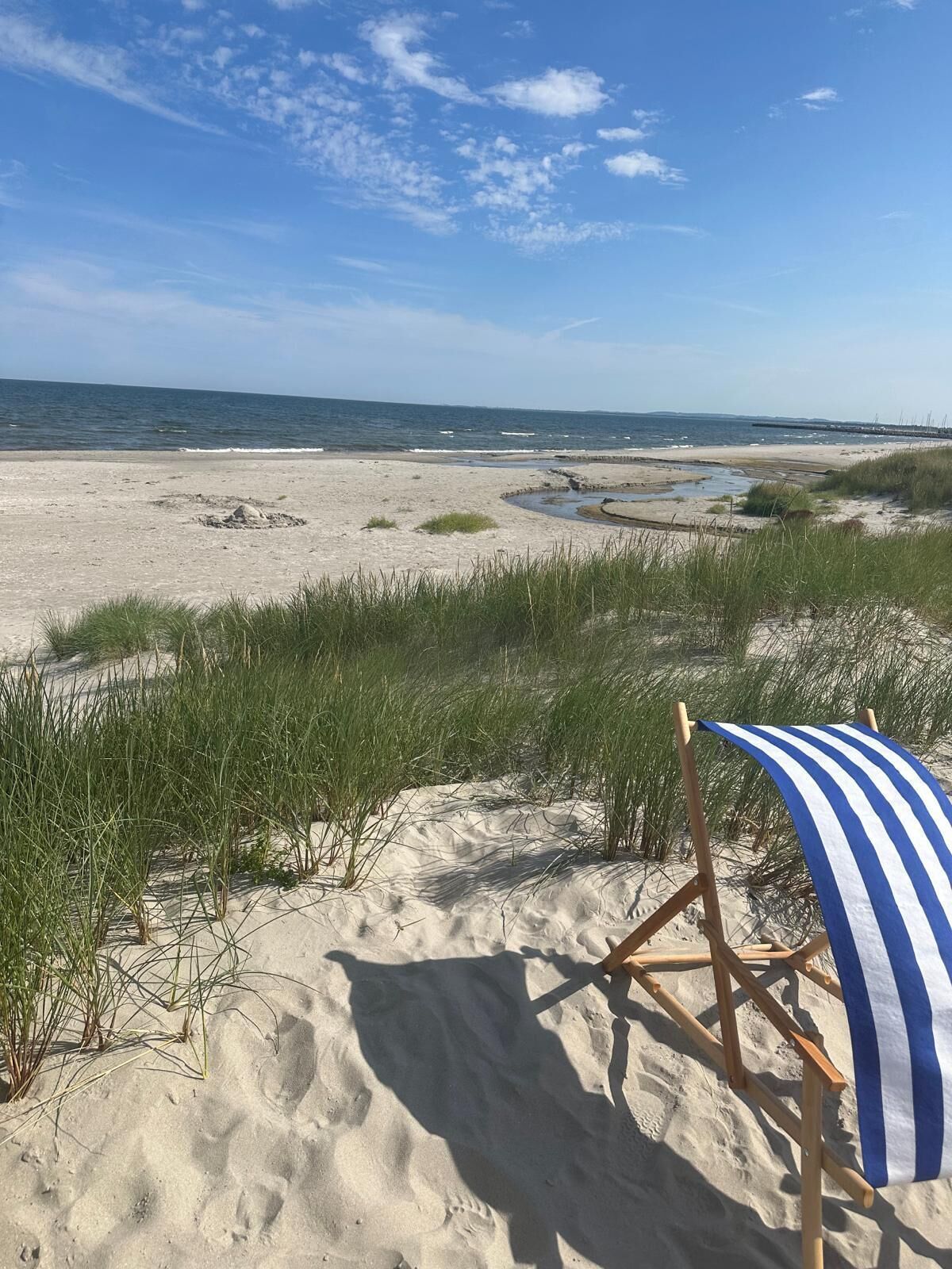 A beach with a blue and white striped beach chair and a sandy area with grass.