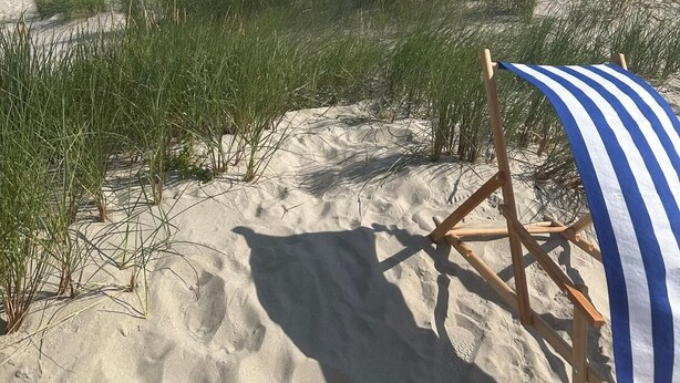 A beach with a blue and white striped beach chair and a sandy area with grass. - Panoramic ocean view, direct access to a private sandy beach in Skagen South—family-friendly (Ålbæk)