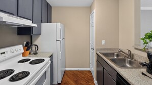 A compact kitchen with a white stove, a refrigerator, dark cabinets, a granite countertop, and a sink. - Kingsgate One Bedroom Stay (Beaumont)