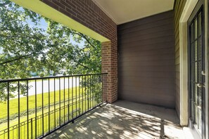 Un balcon avec une balustrade en métal, un mur en briques et une vue sur un champ verdoyant.