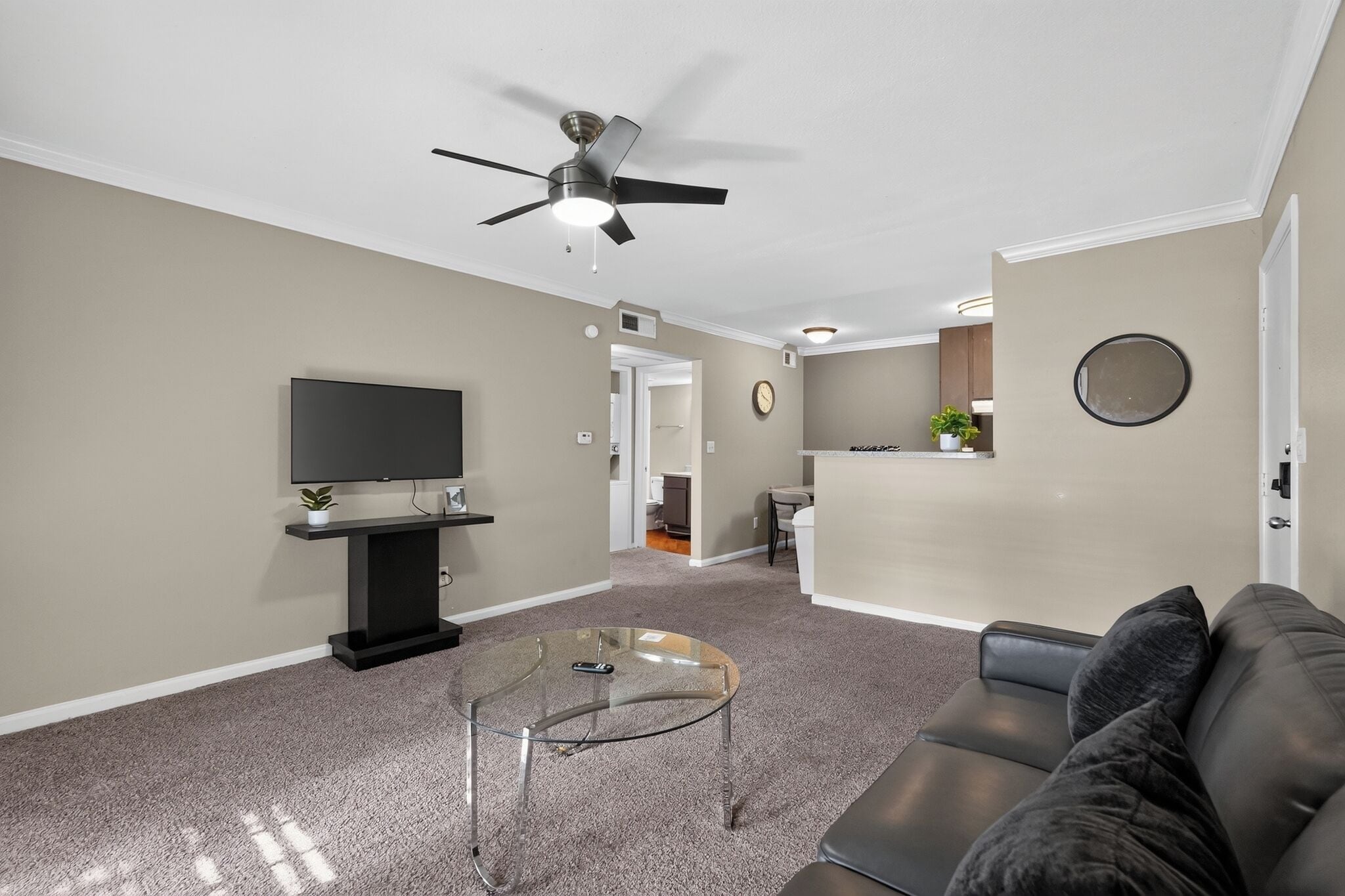Ein Wohnzimmer mit Flachbildfernseher, Glastisch, Sofa und Deckenventilator.