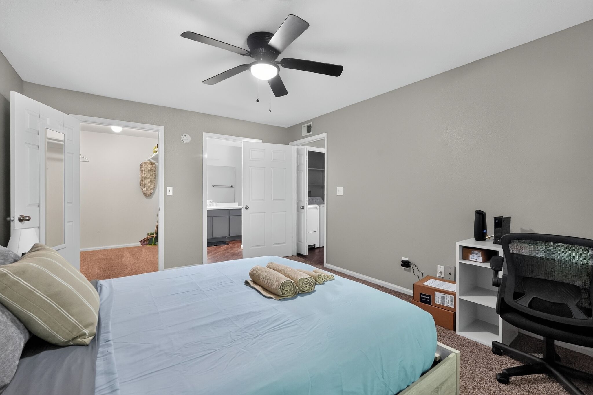 Una camera da letto con un letto, una ventola a soffitto, una scrivania con un computer e una sedia.