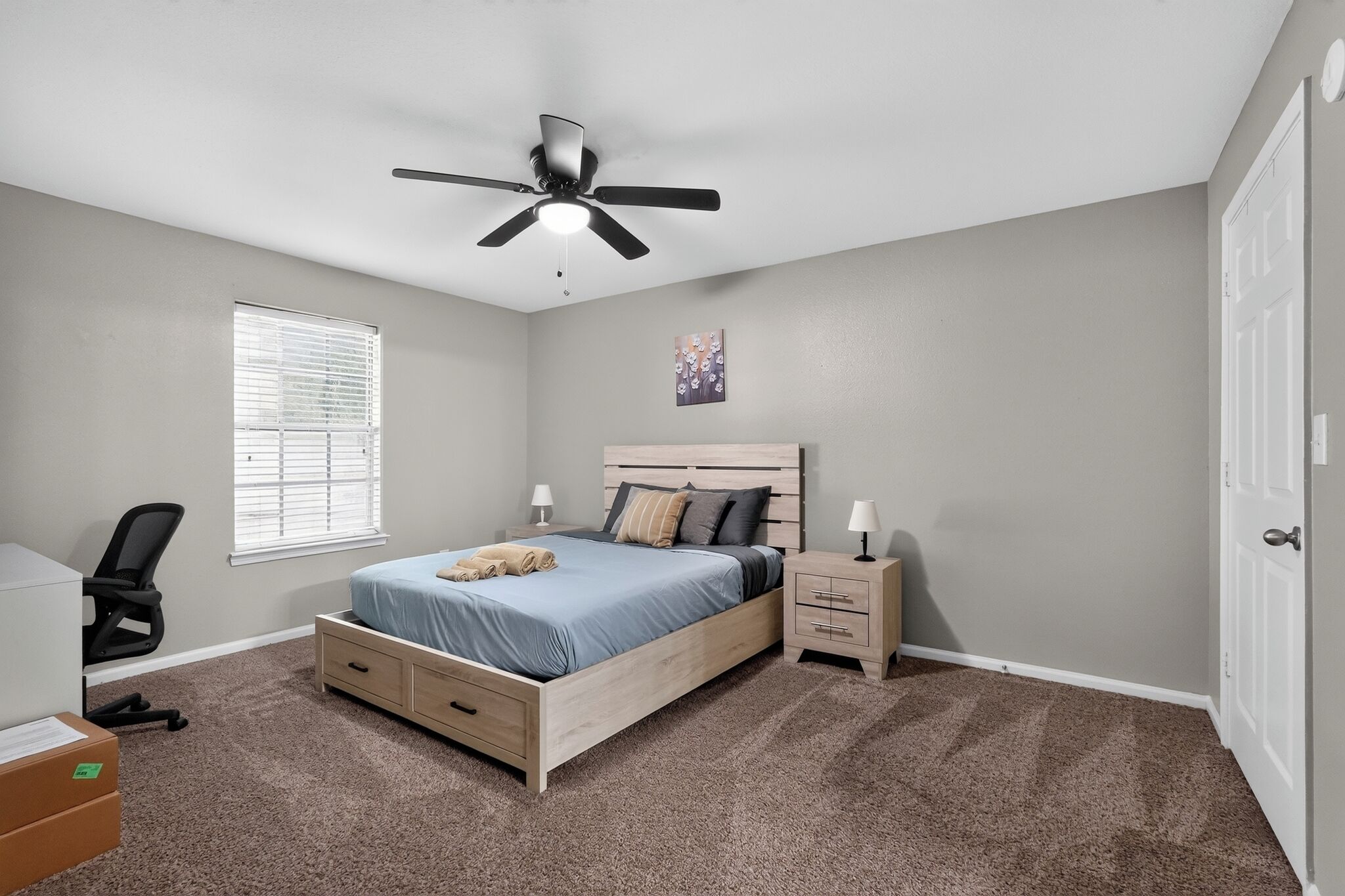 A bedroom with a bed, bedside tables, a ceiling fan, a window with blinds, and a door.