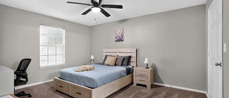 A bedroom with a bed, bedside tables, a ceiling fan, a window with blinds, and a door.