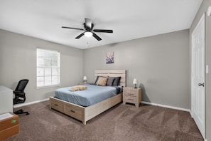 A bedroom with a bed, bedside tables, a ceiling fan, a window with blinds, and a door.