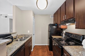 A compact kitchen with a granite countertop, stainless steel sink, a black refrigerator, and a black stove.