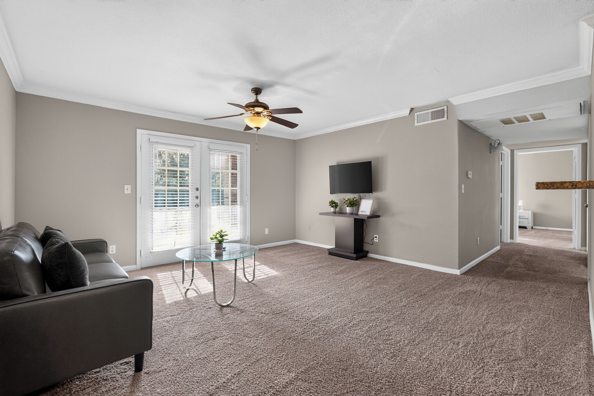 A living room with a sofa, a glass coffee table, a ceiling fan, and a TV on a stand.
