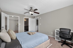 A bedroom with a bed, a ceiling fan, a desk with a chair, and a walk-in closet.