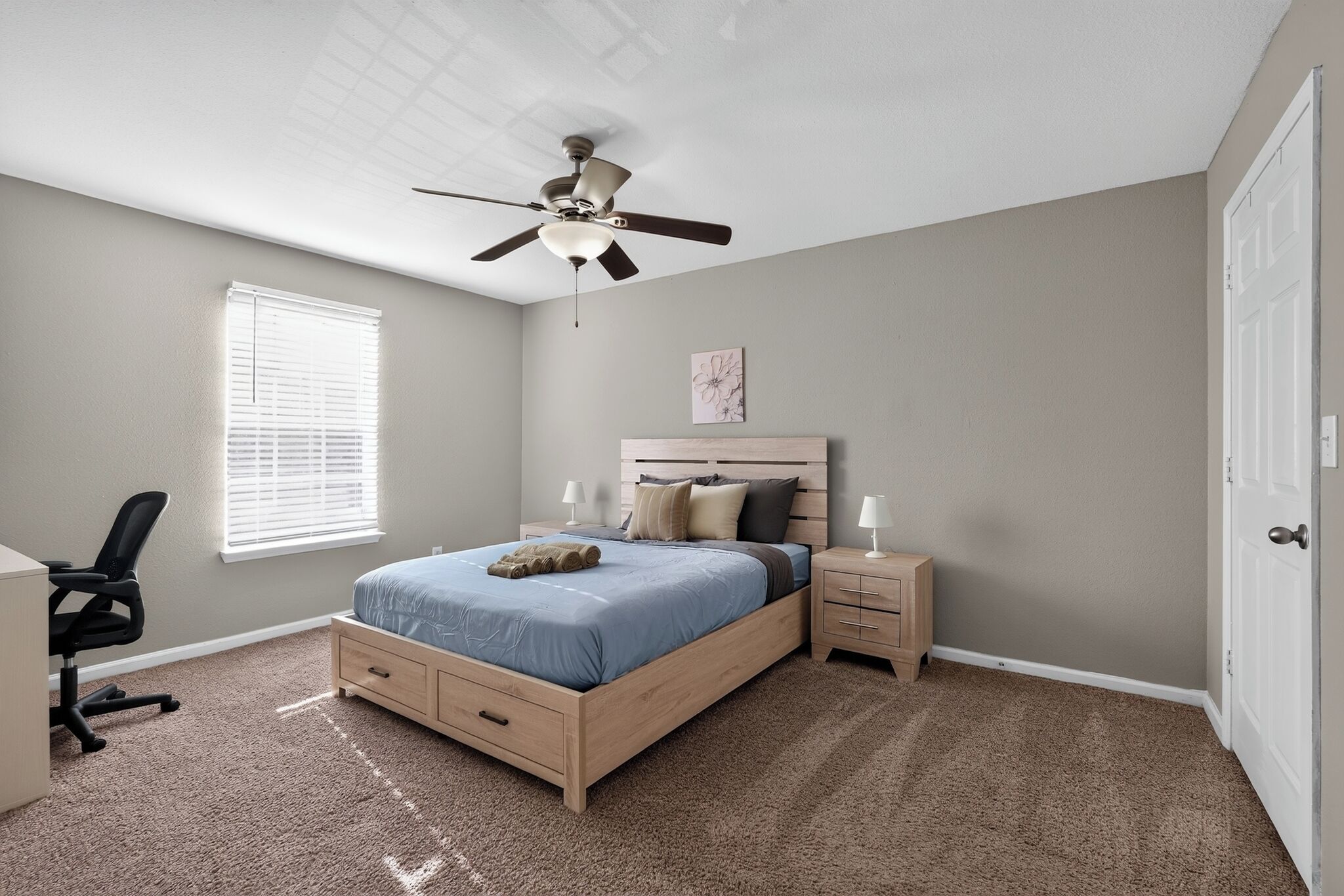 A bedroom with a bed, bedside tables, a desk, and a ceiling fan.