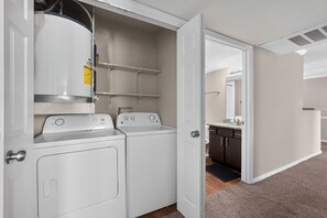 A laundry area with two front-loading washers and dryers, a white door, and a view into a bathroom with a dark countertop and cabinets. - Relaxing Kingsgate 2BR (Beaumont)