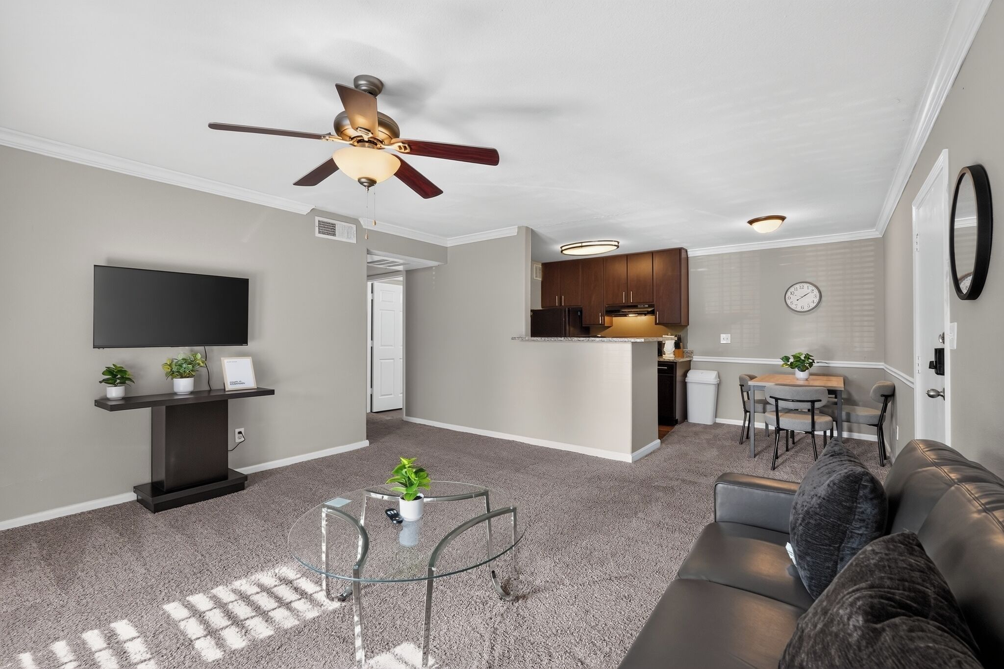 A modern living room with a flat-screen TV, a glass coffee table, a sofa, and a ceiling fan.