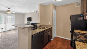 A compact kitchen with a built-in dishwasher, a sink, and a black refrigerator. - Relaxing Kingsgate 2BR (Beaumont)