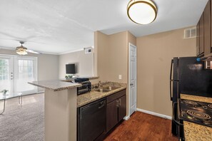 A compact kitchen with a built-in dishwasher, a sink, and a black refrigerator. - Relaxing Kingsgate 2BR (Beaumont)