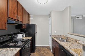 A compact kitchen with wooden cabinets, a black stove, a microwave, and a stainless steel sink.