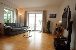 Ein Wohnzimmer mit einer Couch, einem Couchtisch, einem Fernseher und einer Pflanze.