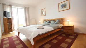 A bedroom with a bed, a television, a bedside table with a lamp, a dresser, and a window with curtains. - Appartement im Seedomizil Kummerow (Kummerow)