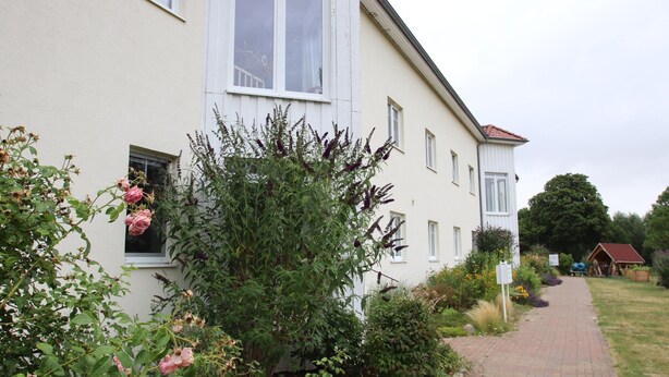 A two-story building with a paved pathway leading to a wooden structure. - Appartement im Seedomizil Kummerow (Kummerow)
