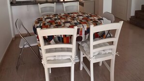 A dining area with a table set for four, white chairs, a patterned tablecloth, and a ceiling light fixture.