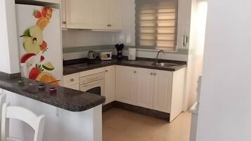 A kitchen with white cabinets, a countertop, a sink, and a window with blinds.
