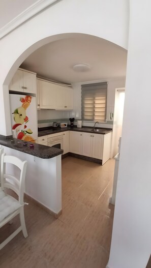 A kitchen with white cabinets, a countertop, a sink, and a window with blinds.