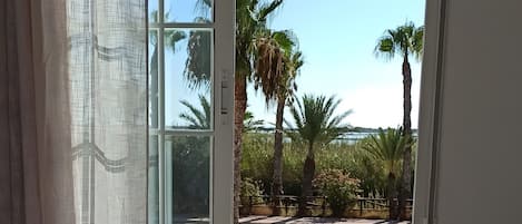Una habitación con cama, ventana y cortina, con vistas a palmeras.