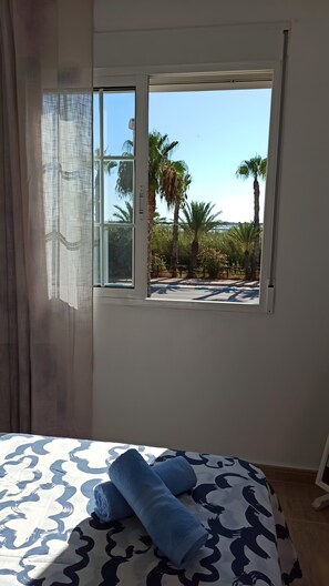 A room with a bed, a window with a view of palm trees, and a curtain.