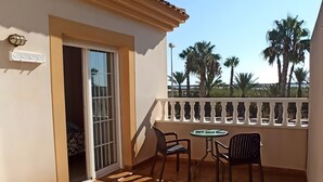 A balcony with a tiled floor, a table with chairs, and a view of palm trees.
