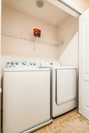 A laundry room with two front-loading washers and dryers, a shelf with laundry detergent, and a door to the right. - Tranquil Vacations (Kissimmee)
