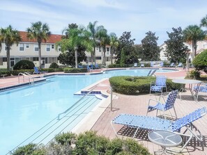 A swimming pool with lounge chairs and a small table, surrounded by palm trees and buildings. - Tranquil Vacations (Kissimmee)