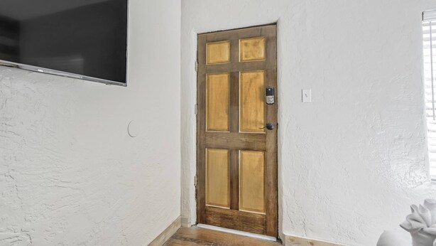 Una stanza con una porta in legno, un muro bianco e strutturato, e una piccola finestra con persiane.