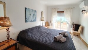 Ett sovrum med en säng, en lampa, en tavla och utsikt över naturen.