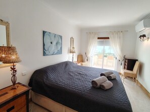 Ein Schlafzimmer mit einem Bett, einer Lampe, einem Bild und Blick ins Freie.