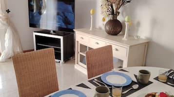 A dining area with a television, wicker chairs, a white table with blue plates, and a variety of food items.