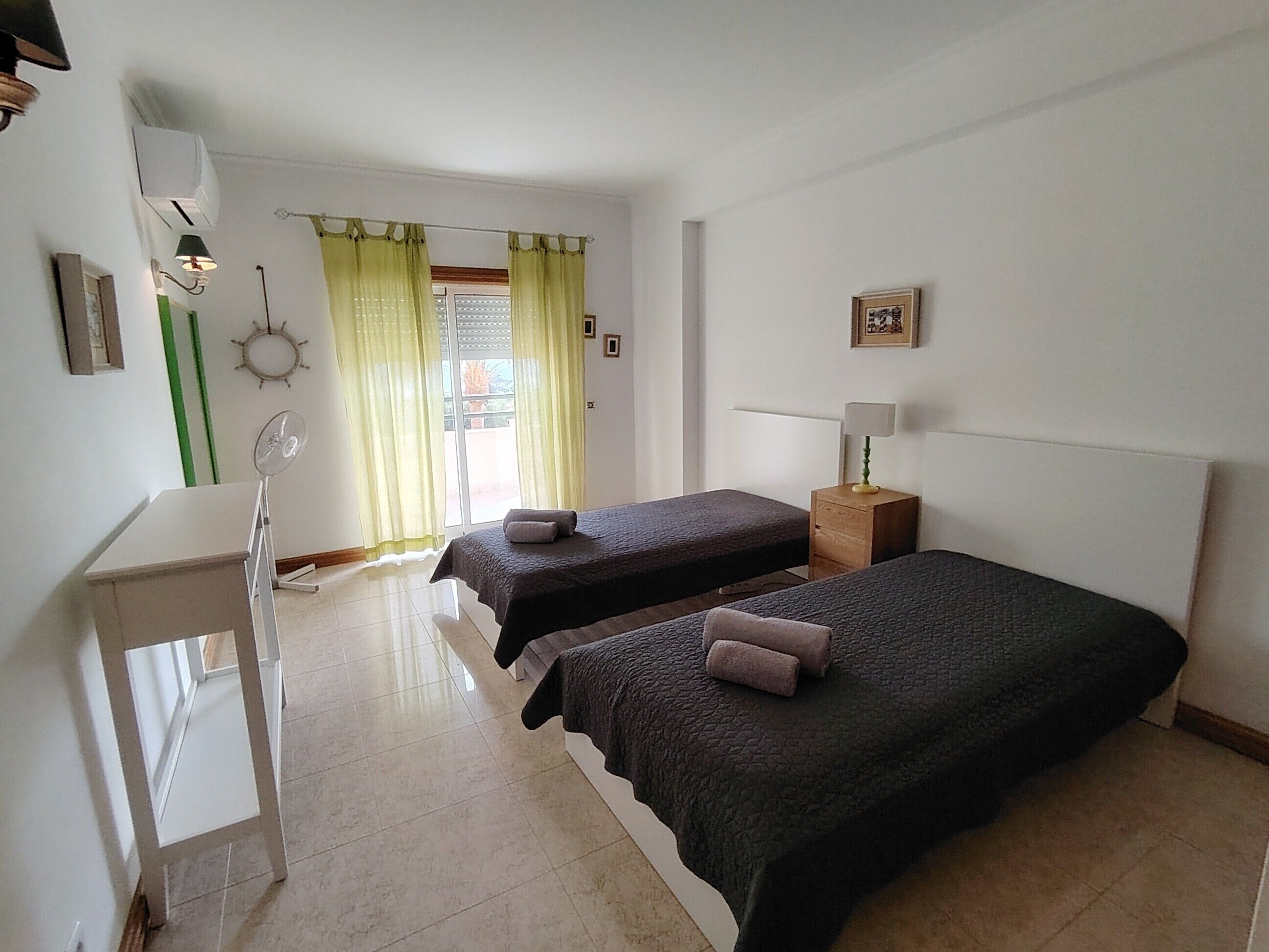 A room with two beds, a desk, a chair, a lamp, and a window with curtains.