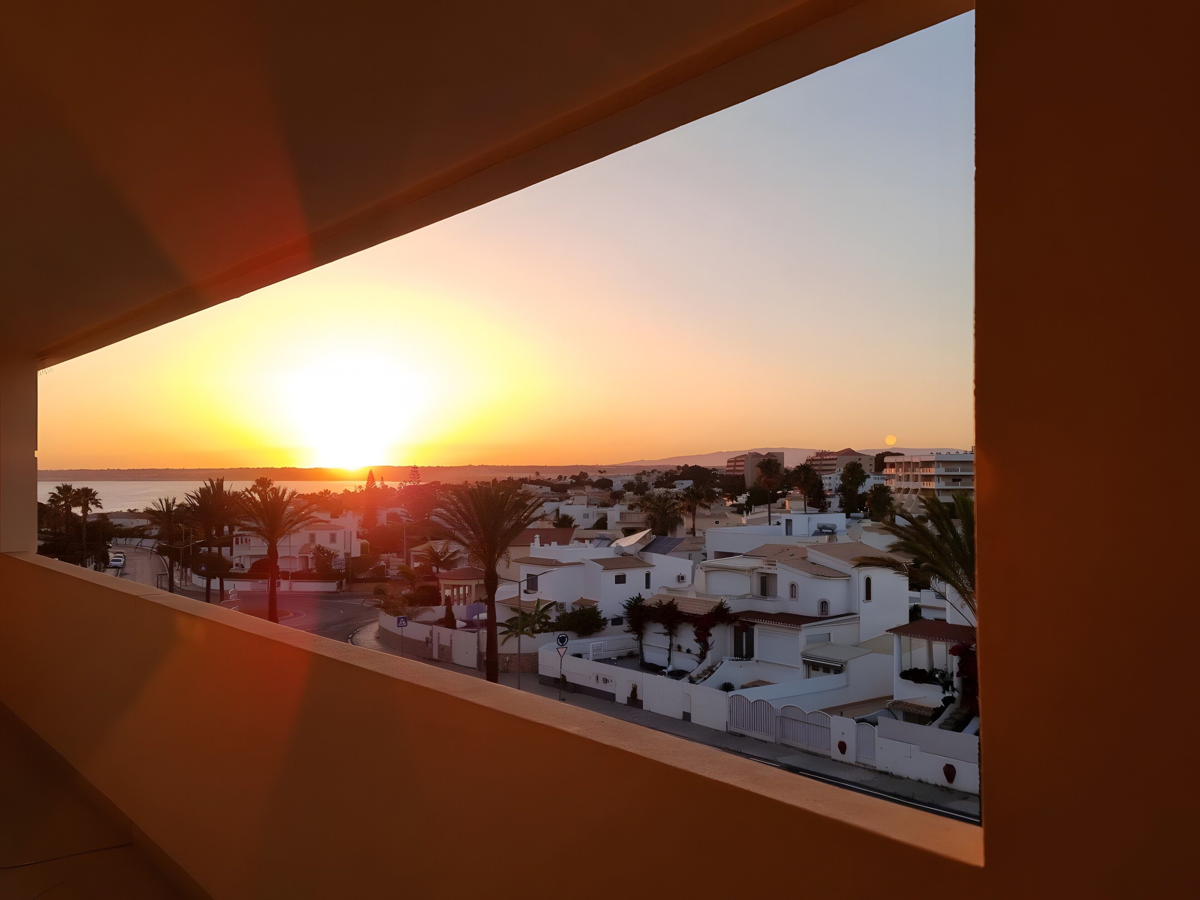A coastal town at sunset with white buildings and palm trees.