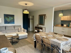 Un salon moderne comprenant un canapé, une table à manger et des chaises, un coin cuisine et un grand tableau accroché au mur.