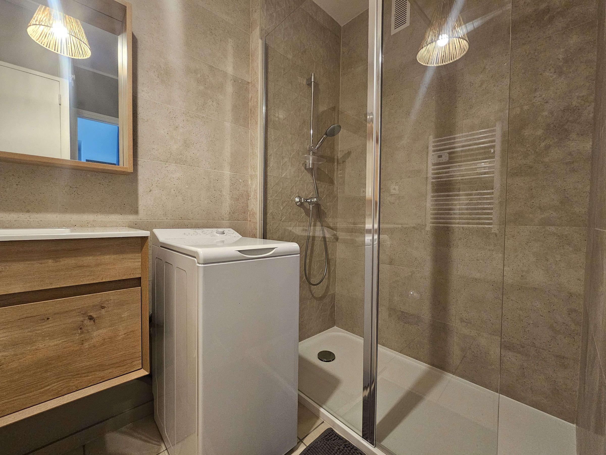 A modern bathroom with a glass-enclosed shower, a built-in washing machine, and a wooden vanity.
