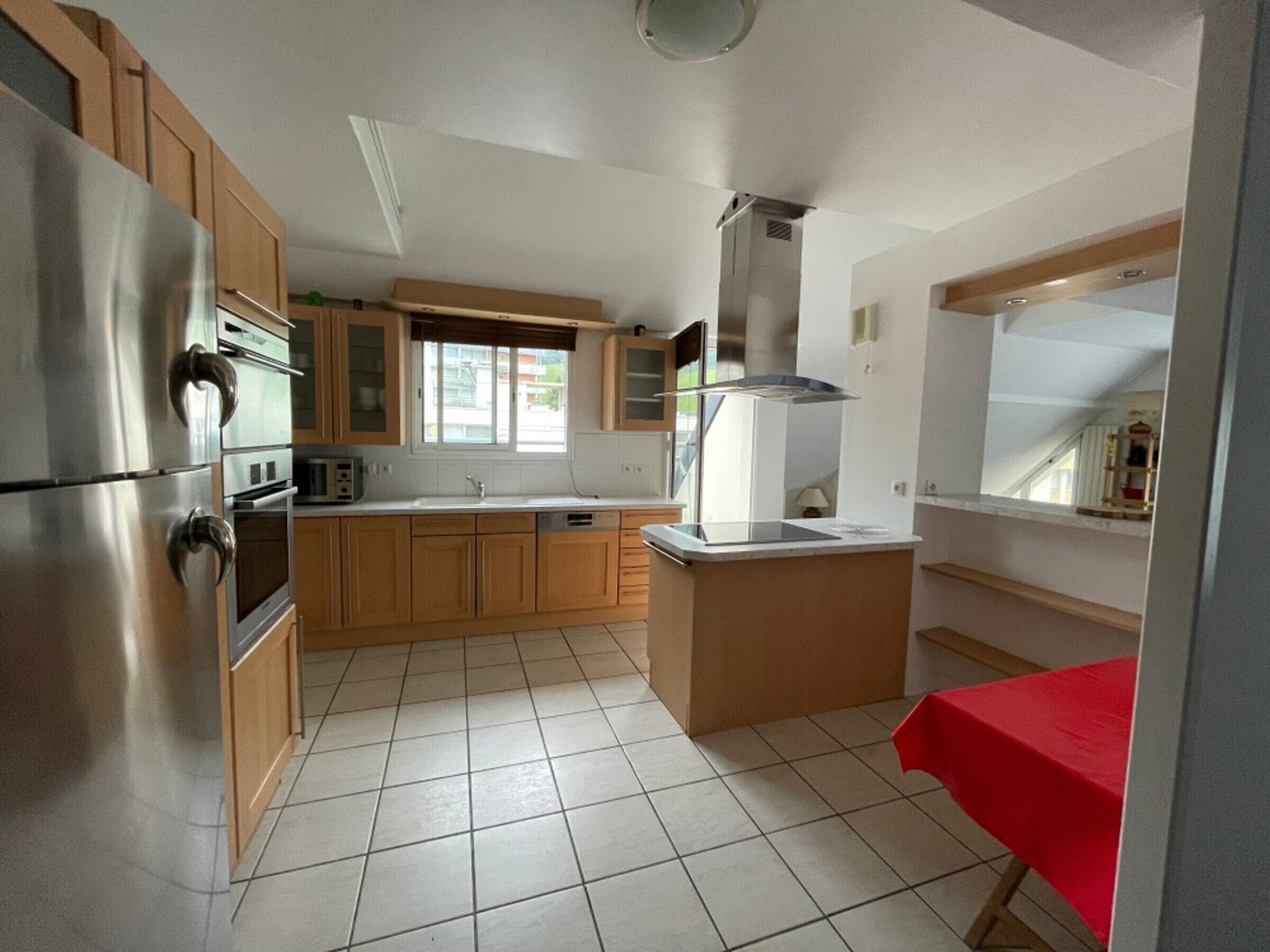 A kitchen with stainless steel appliances, wooden cabinets, a window, and a tiled floor.