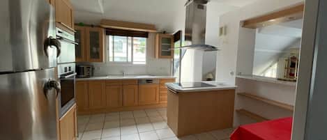 A kitchen with stainless steel appliances, wooden cabinets, a window, and a tiled floor.