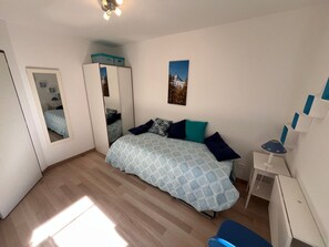Ein Schlafzimmer mit einem Bett, einem Schreibtisch, einem Spiegel und einem Bild an der Wand.