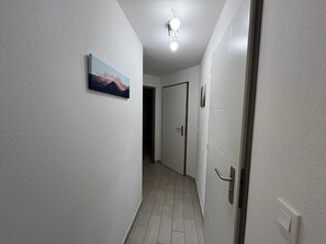 Ein Flur mit einer Tür am Ende, einer Deckenleuchte und einem Bild an der Wand.