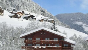 Una cabaña de varios pisos con balcones, rodeada de árboles nevados y montañas.