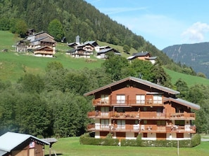 A multi-story chalet with balconies, set in a mountainous area with other similar buildings. - Charming apartment at the foot of the slopes - 6 guests (Arêches-Beaufort)