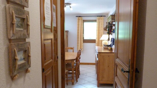 Un pasillo que conduce a un comedor con piso de baldosas, muebles de madera y una ventana con cortinas.