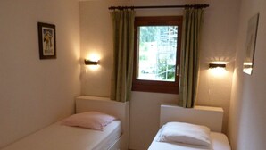 Una habitación pequeña con dos camas individuales, una ventana con cortinas e iluminación en la pared.