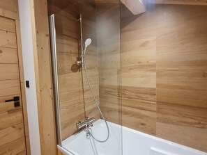 Eine Duschkabine mit Glastür, Handbrause und am Wand montiertem Wasserhahn.