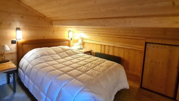 Ein gemütlicher Holzraum mit einem großen Bett, einem Nachttisch, einer Lampe und einer Wandleuchte.
